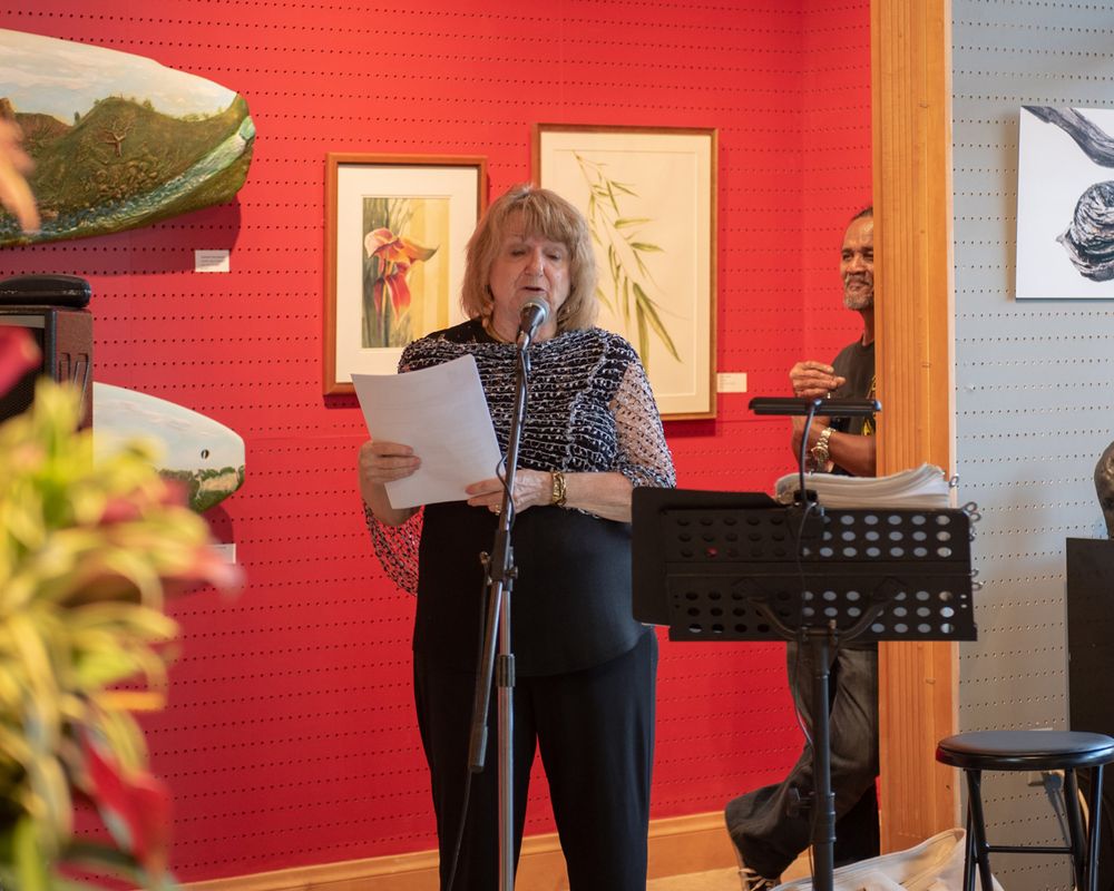 Speaker at a podium presents in front of red wall with artwork in a gallery setting.