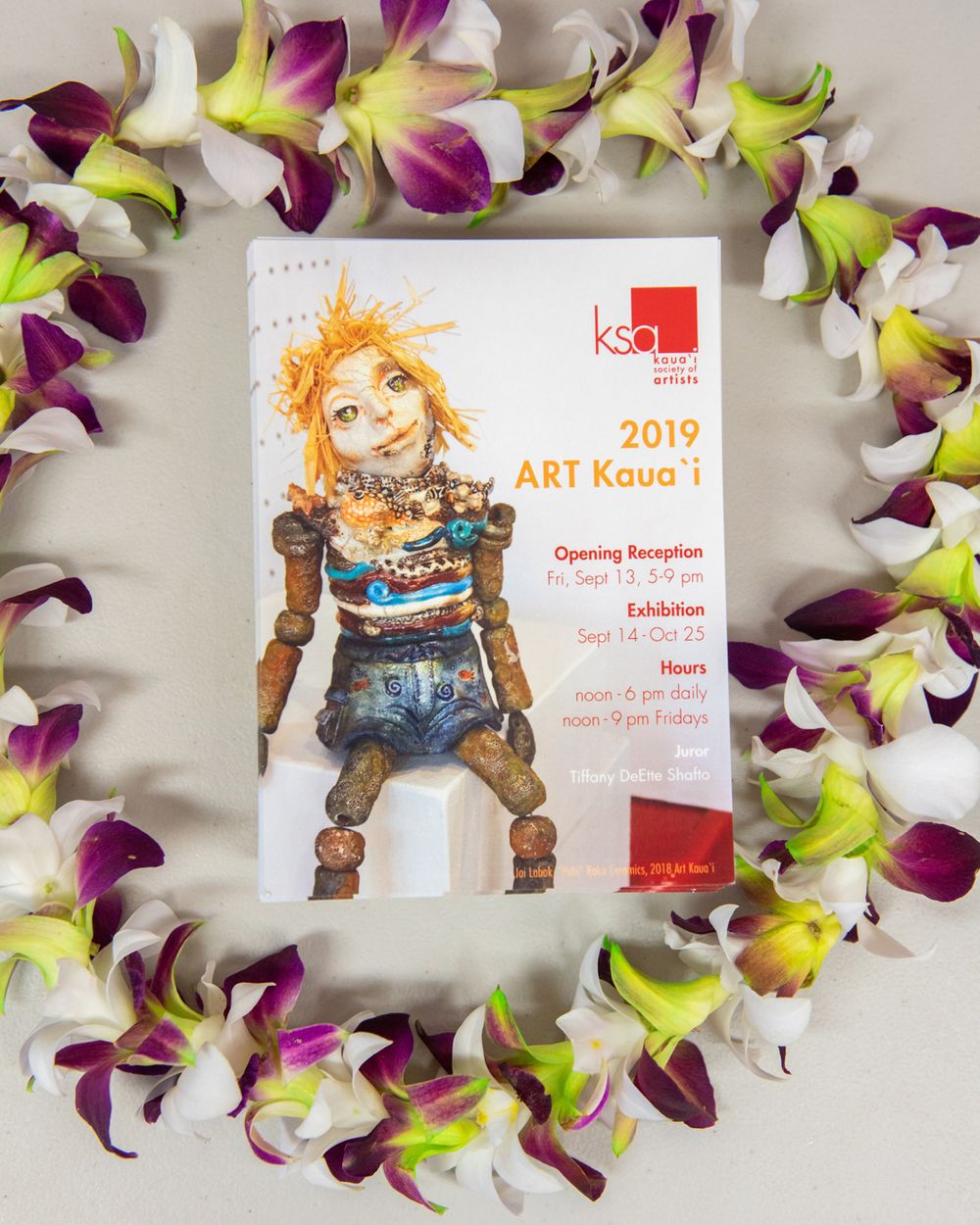 2019 Art Kaua'i exhibition program surrounded by colorful orchid lei.
