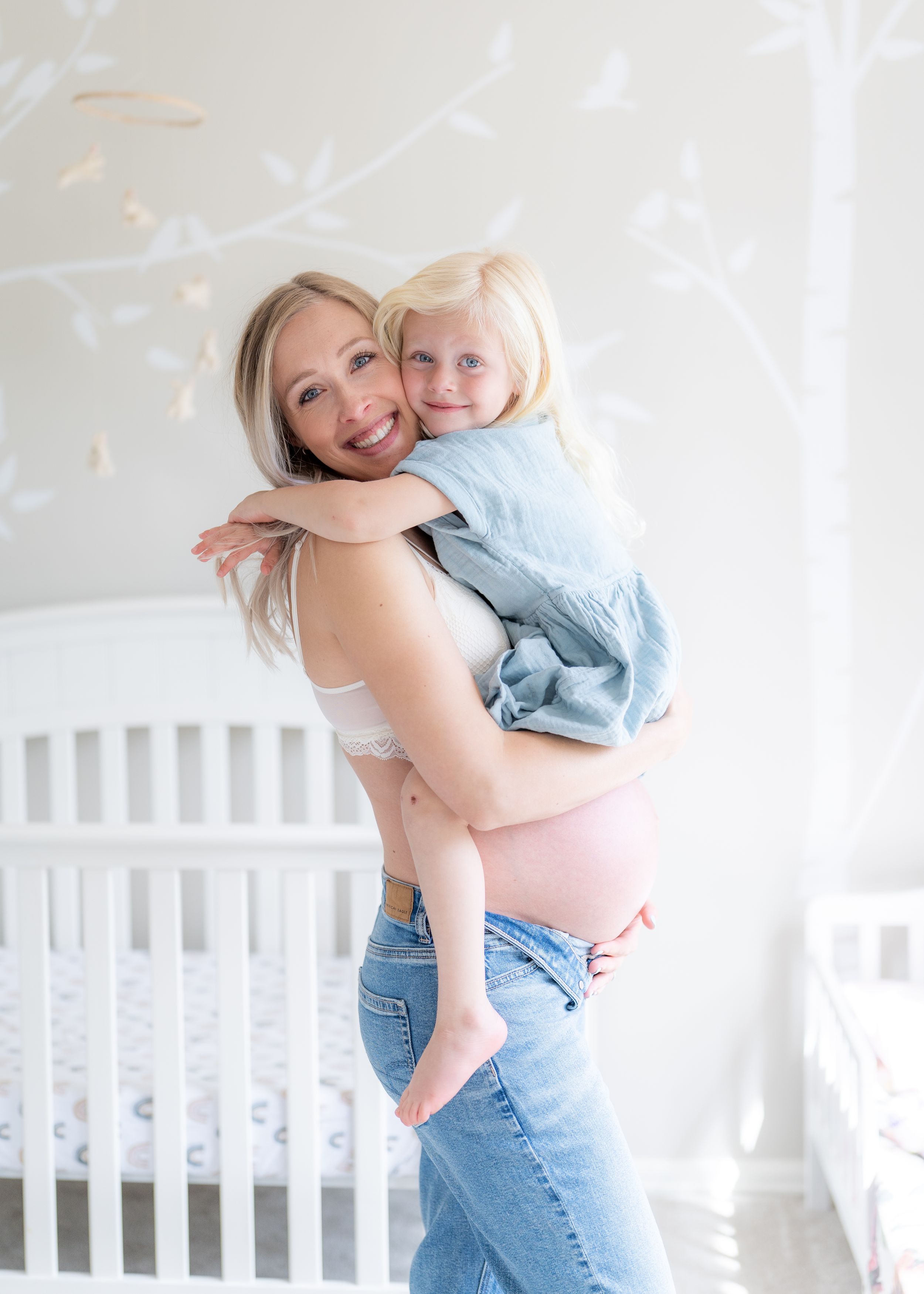 Maternity photo of pregnant mother and her young child hugging in nursery.