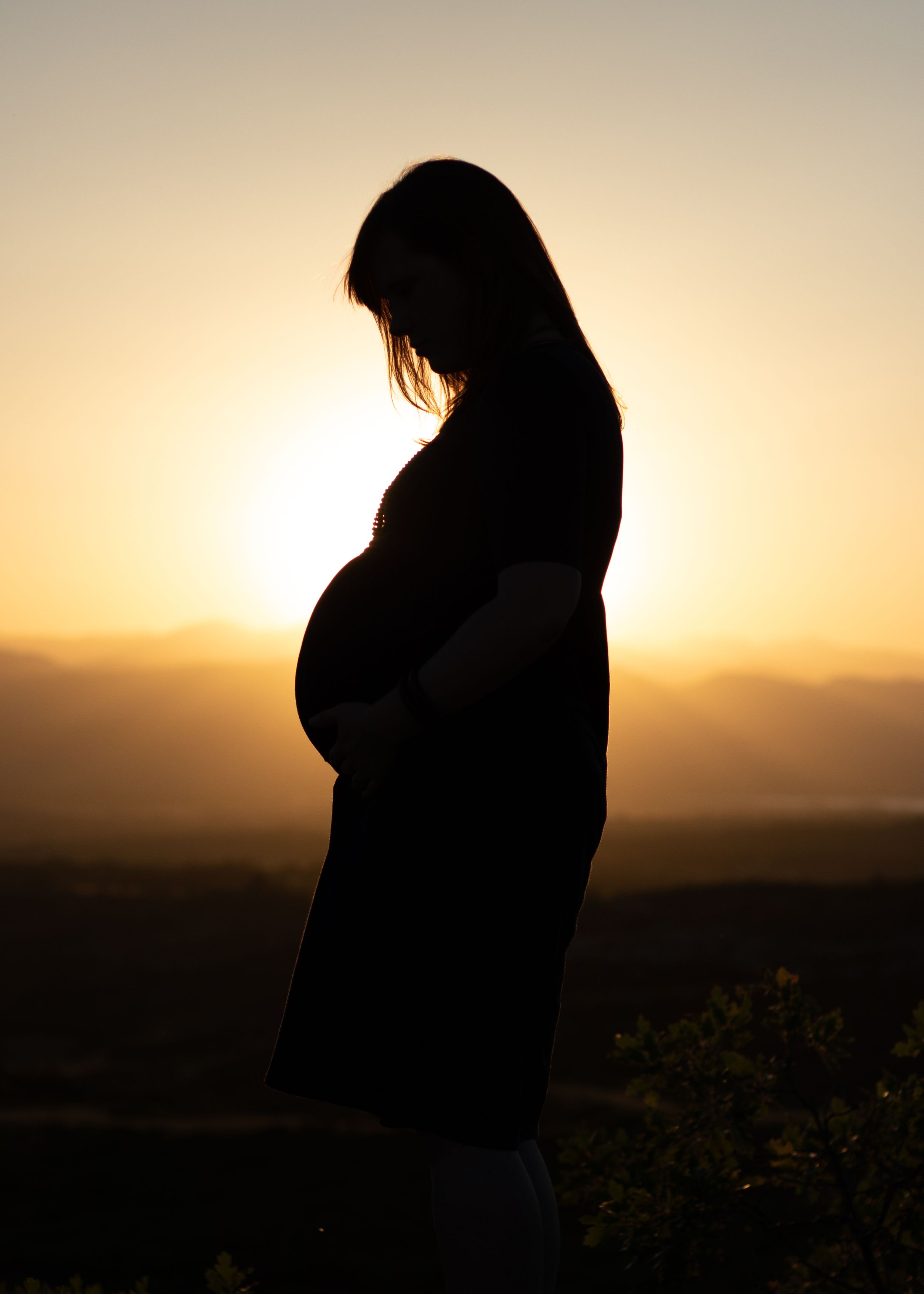 Silhouette of pregnant woman standing against golden sunset sky.