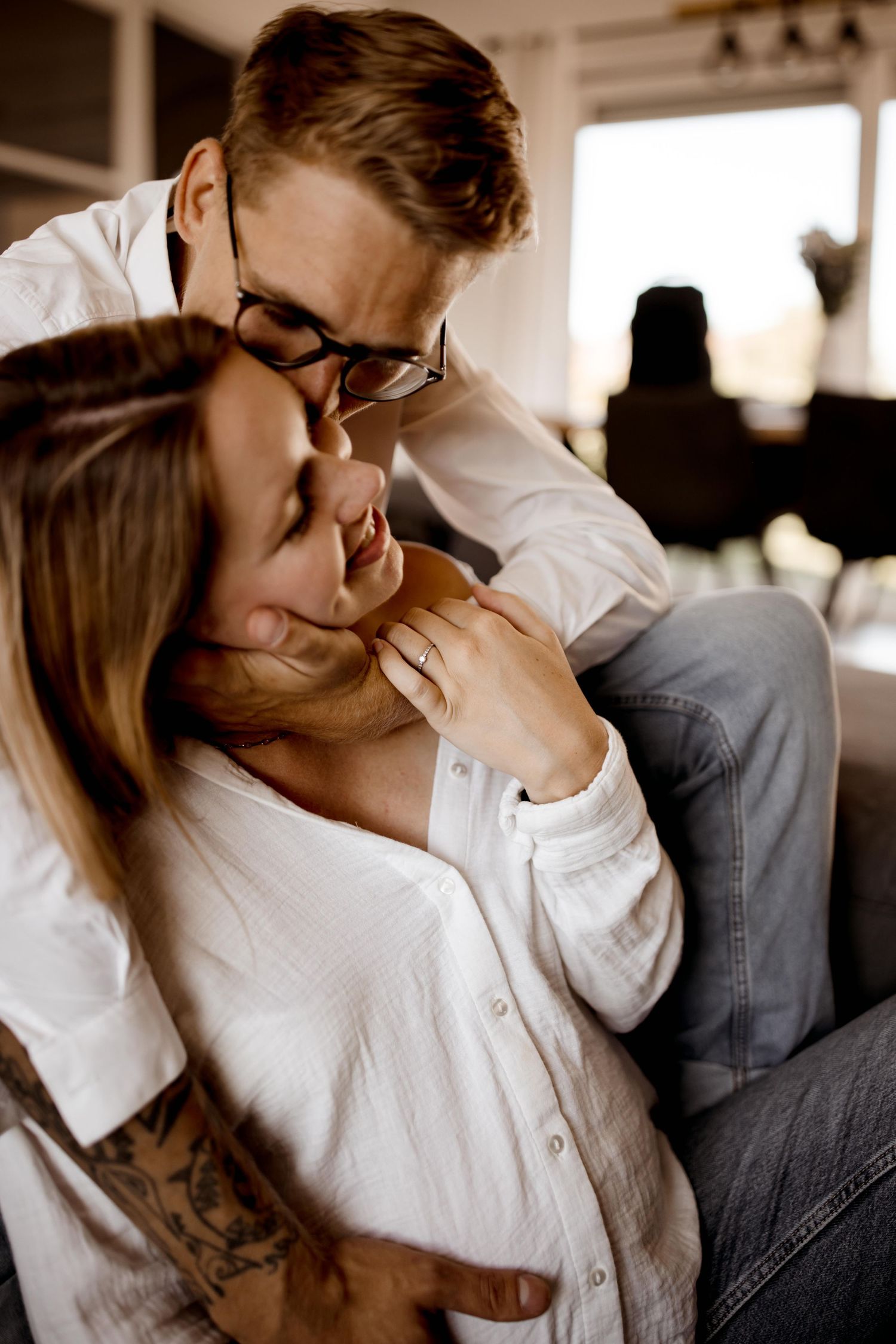 Portrait de style de vie intime d'un couple partageant un moment de tendresse sur un canapé à la lumière naturelle d'une fenêtre.
