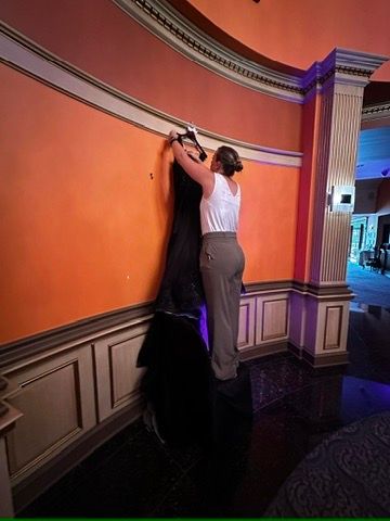 Person hanging black dress on orange wall in elegant venue with white wainscoting and purple lighting.