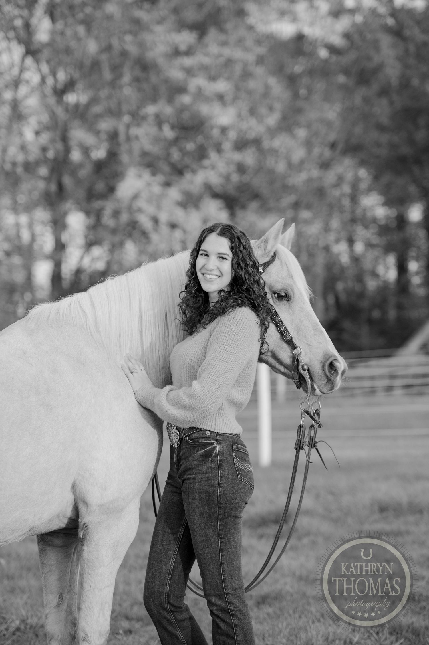 A black and white portrait of someone standing beside a light-colored horse with bridle.
