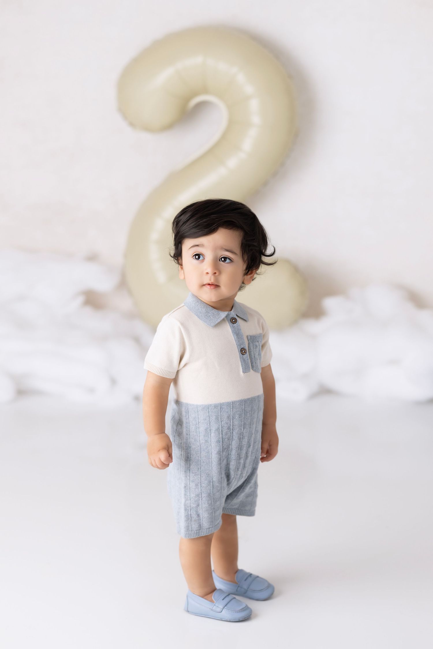 White and blue kids outfit with pale number 2 balloon decoration in neutral studio backdrop for birthday photoshoot.
