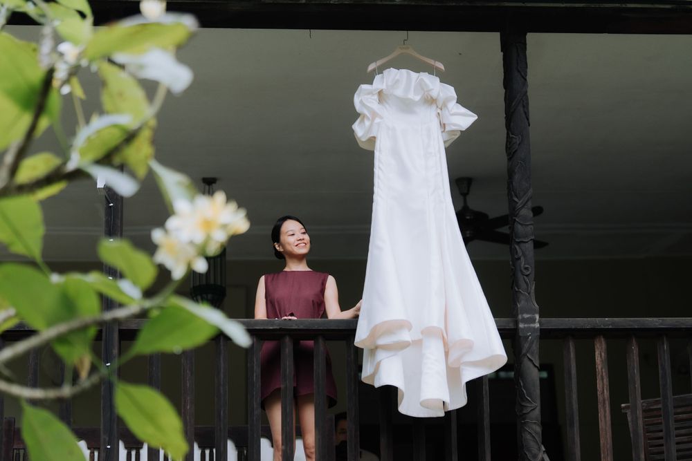 White wedding dress hangs from rustic porch railing beside delicate white blossoms in spring.