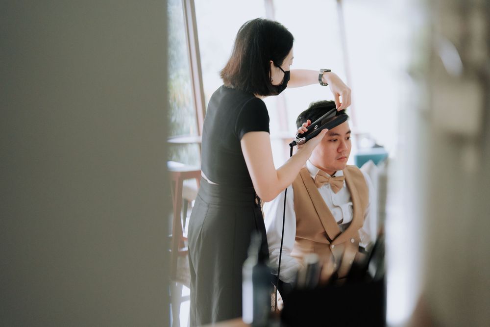 A stylist works on preparing a client's hair in a bright, window-lit space.