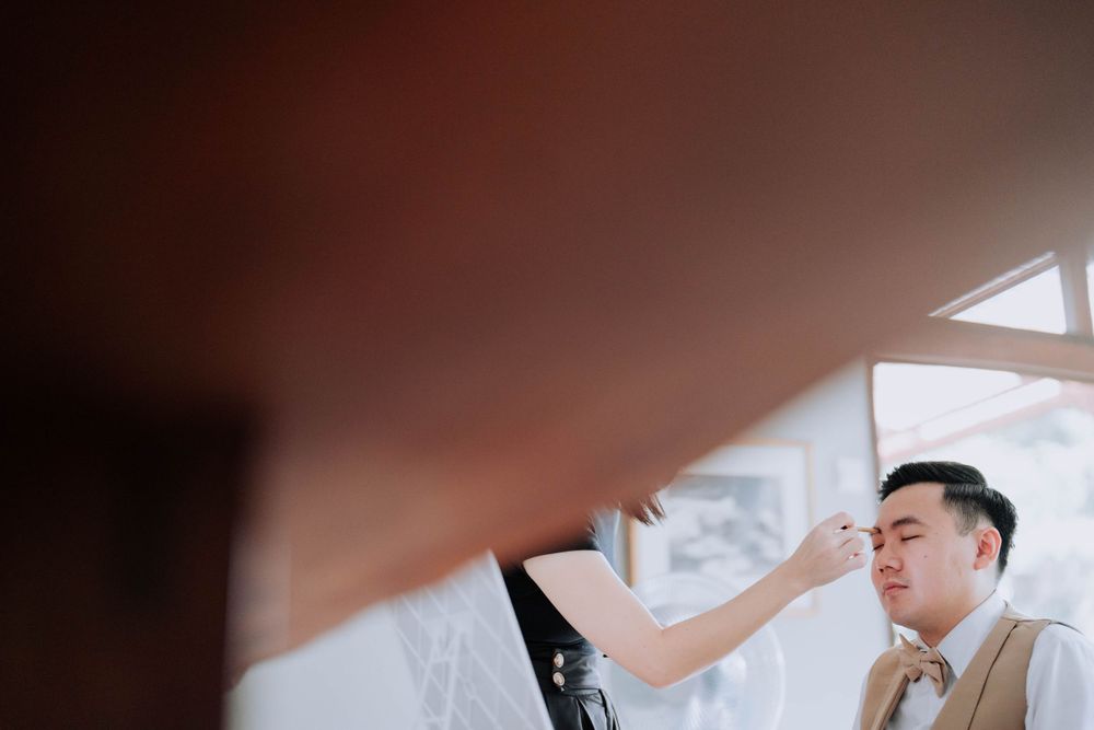 Someone getting their makeup professionally done while wearing a beige vest in a warm-lit indoor setting.