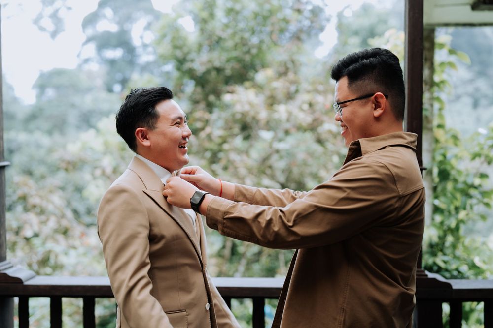 Two men in tan suits engage in a playful altercation on an outdoor deck surrounded by greenery.