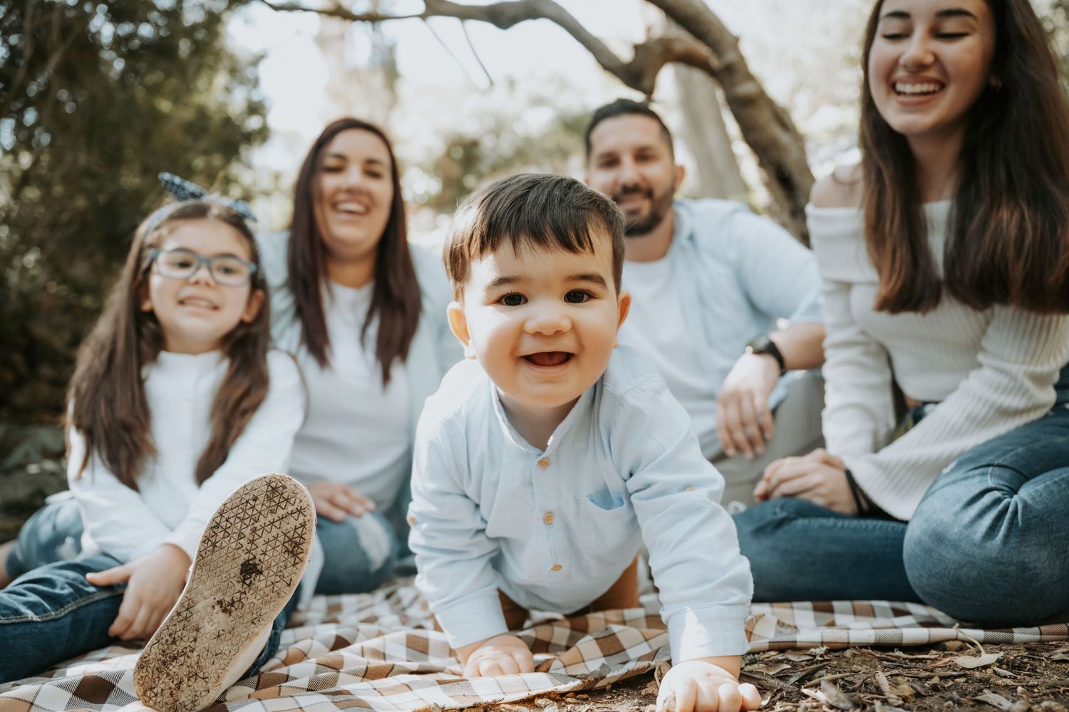 Candid outdoor family photo with young child crawling on picnic blanket.