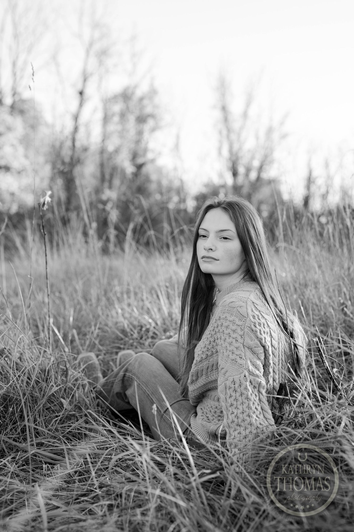 Artistic black and white photo of someone sitting peacefully among tall grass.