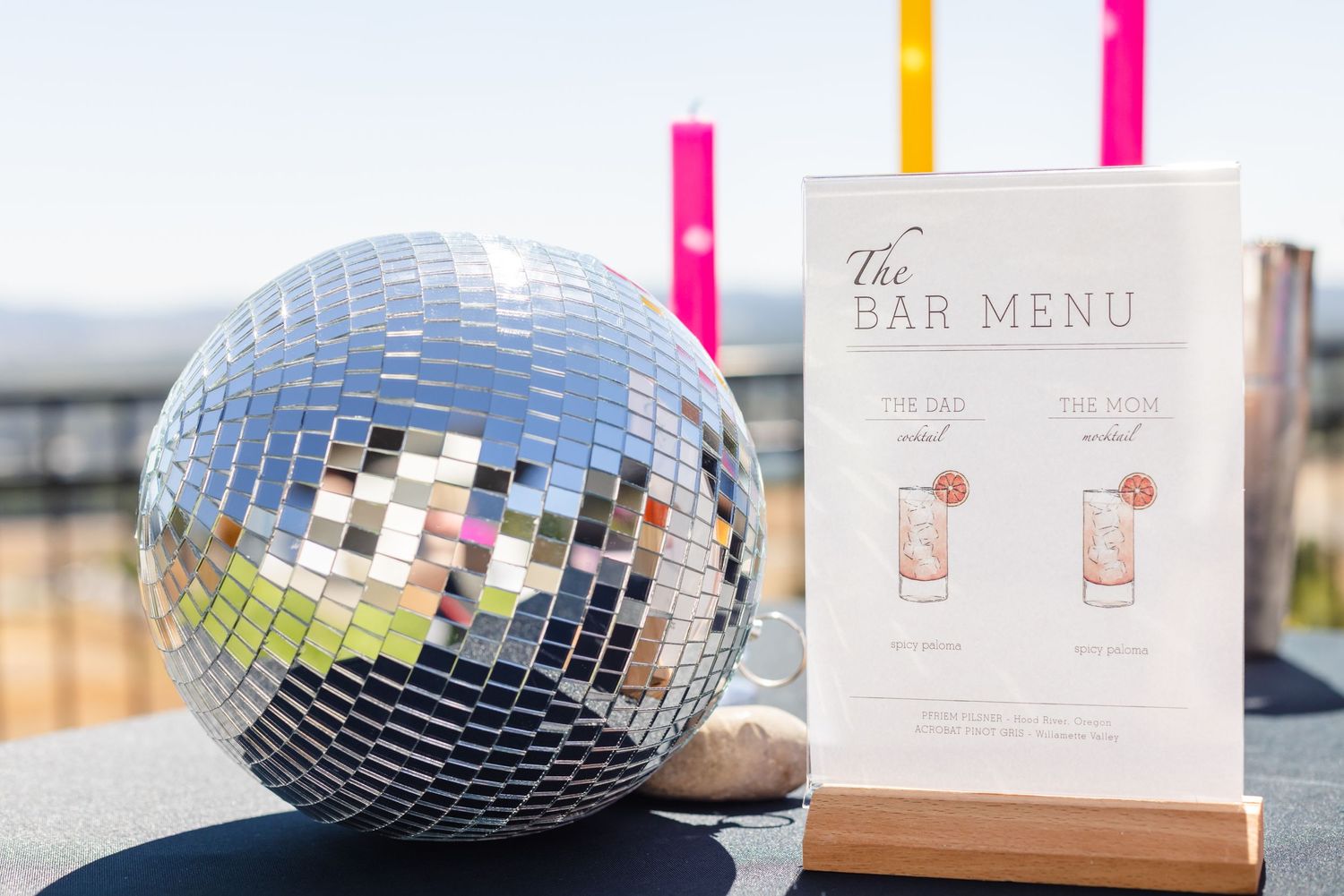 Shiny disco ball next to a bar menu with colorful straws on a black surface.