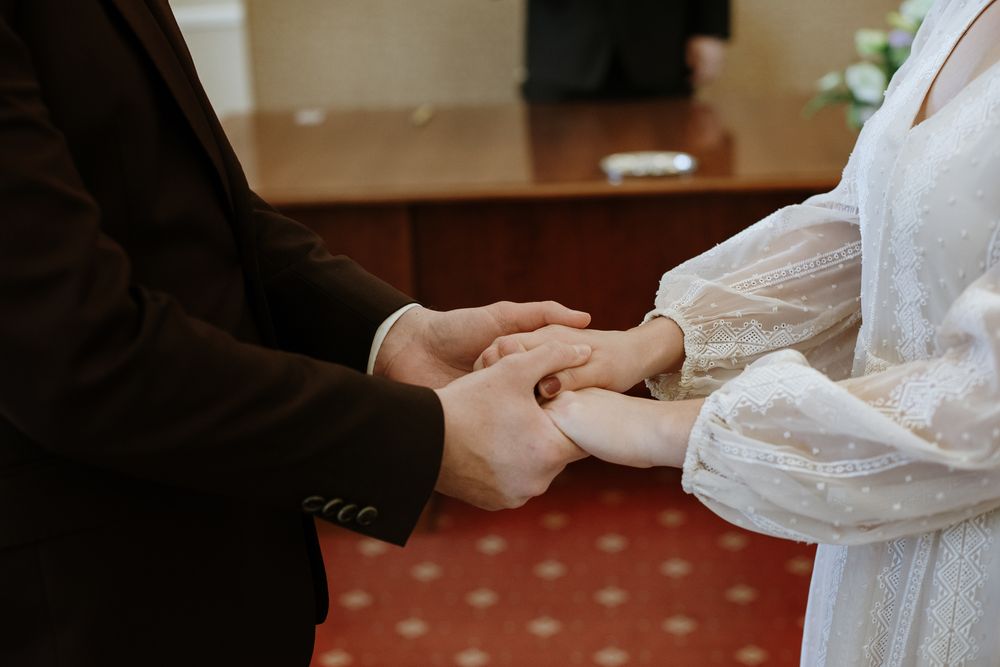 A couple holds hands while dancing together in an indoor venue with red carpeting.