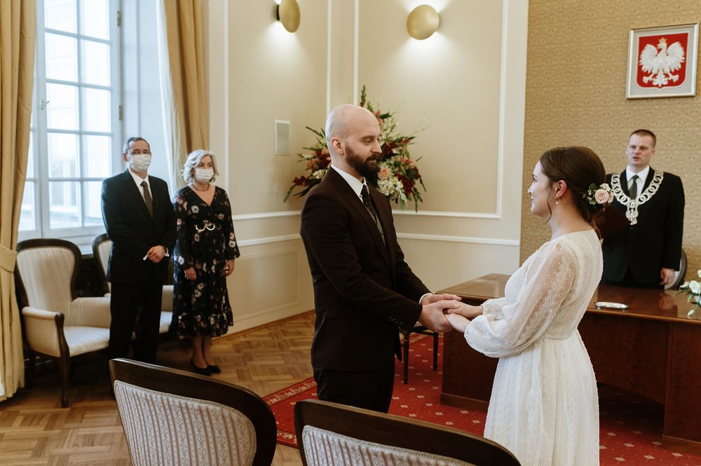 Intimate civil ceremony in a bright room with red carpet and witnesses standing in background during pandemic.