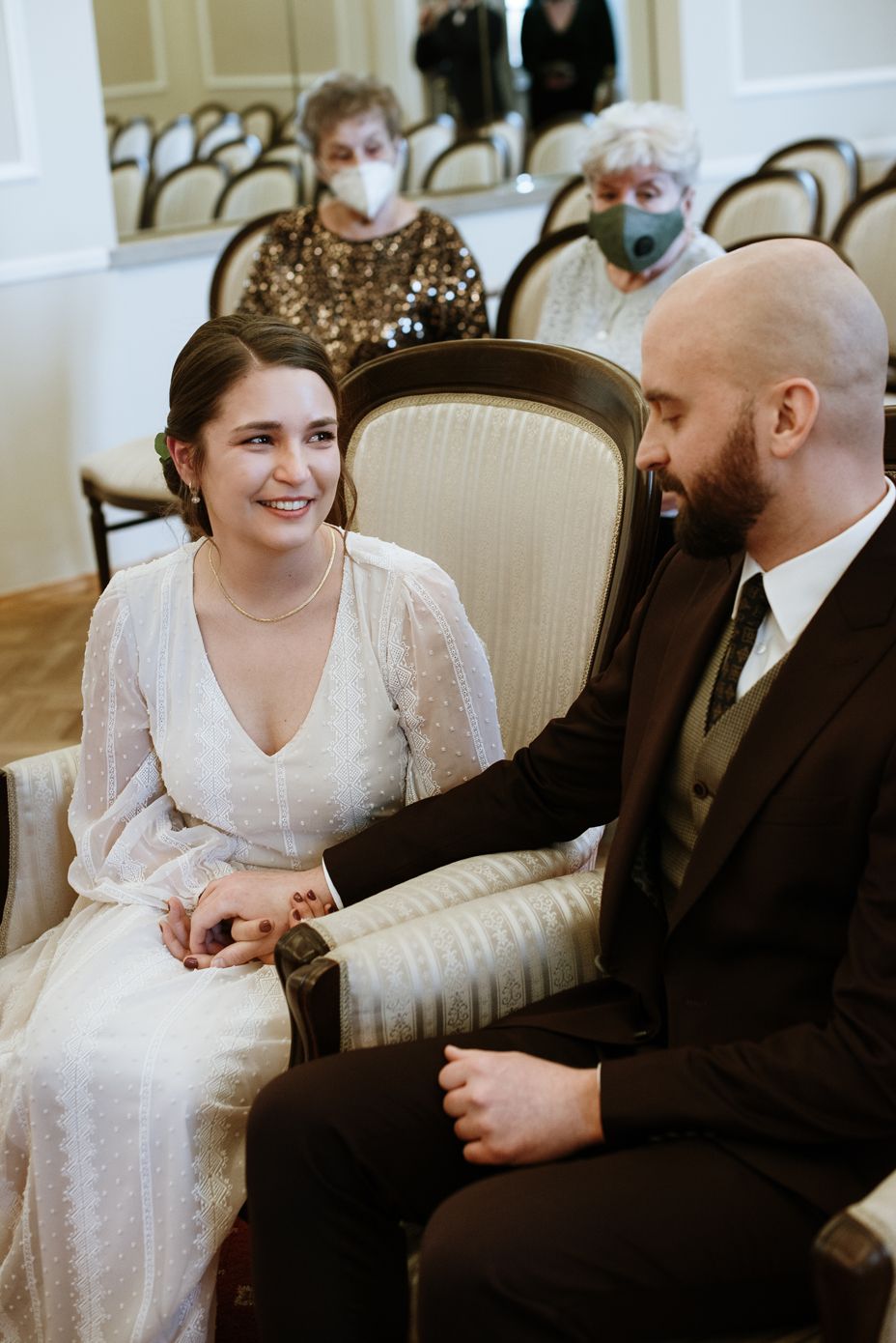 A bride and groom share intimate moments while seated on an elegant striped loveseat during their wedding celebration.