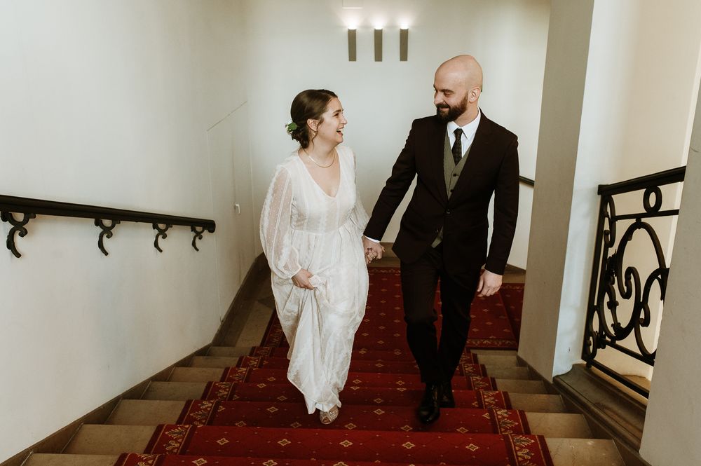 A couple in wedding attire walks down a white hallway with red carpet, photographed from multiple angles.