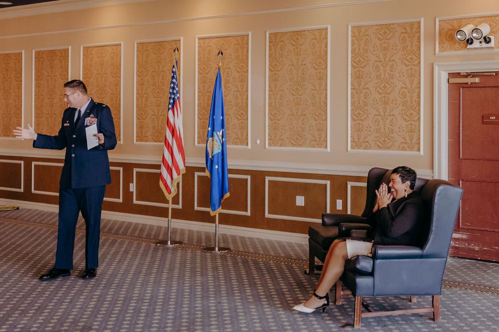 Two people in formal attire meet in an elegant room with American flags on display. Military retirement ceremony.