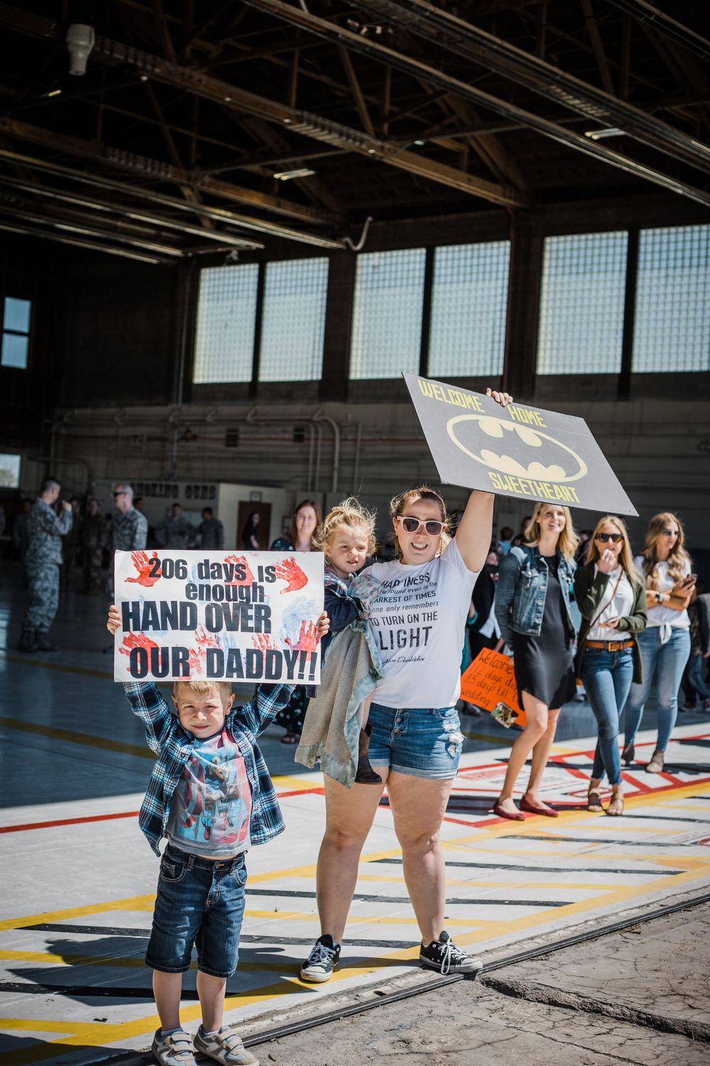 military homecoming, mother and children with signs in hangar, family documentary photography, Whitney Popp