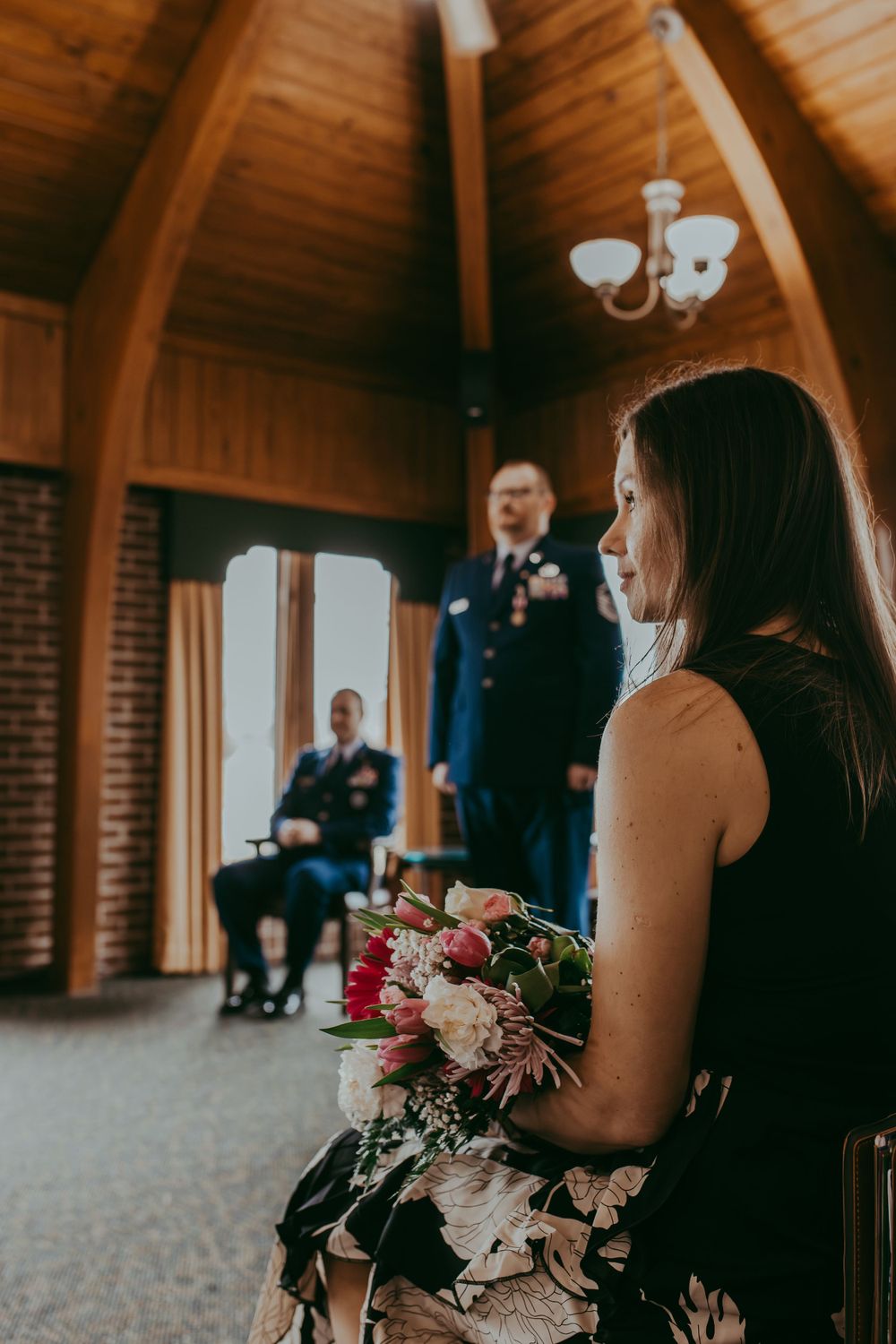A military retirement ceremony in a rustic wooden chapel with vaulted ceilings and a beautiful floral bouquet in the foreground.