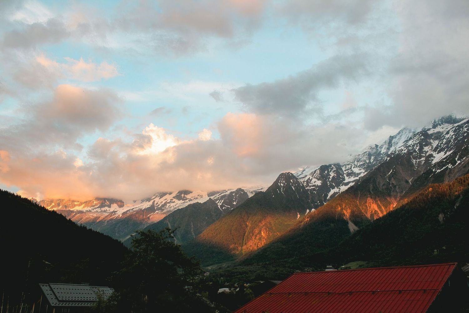 Panoramic view of Aiguille du Midi, Mont Blanc in Chamonix, France, featuring alpenglow on snow-covered peaks and orange sunset clouds.