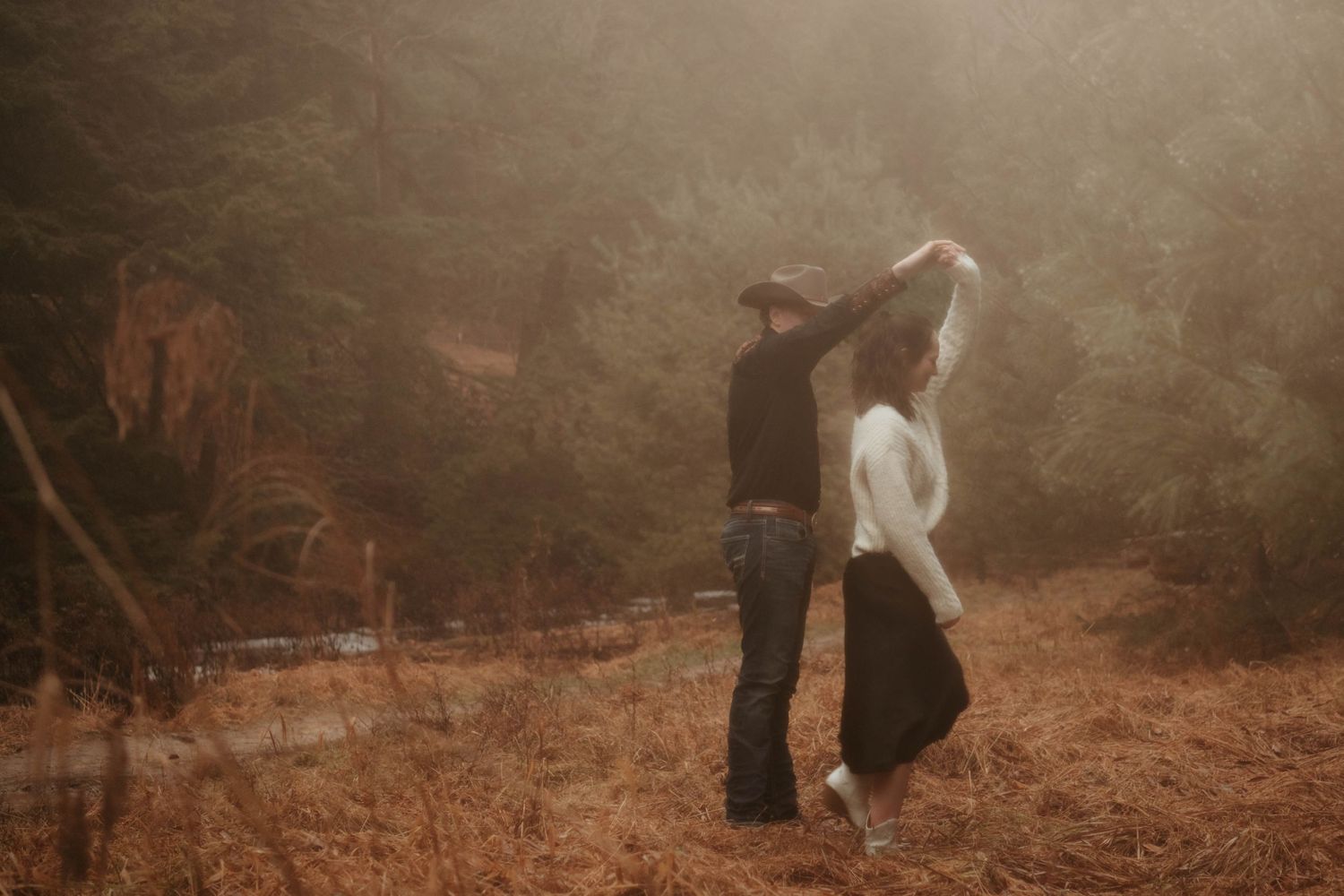 Couple dancing together in misty forest setting during sunset.