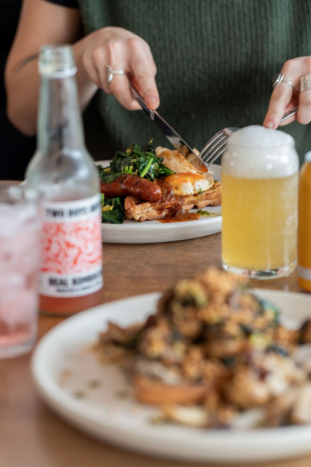 Diners enjoy modern restaurant food and drinks with golden beer and pink beverages served alongside plated dishes.