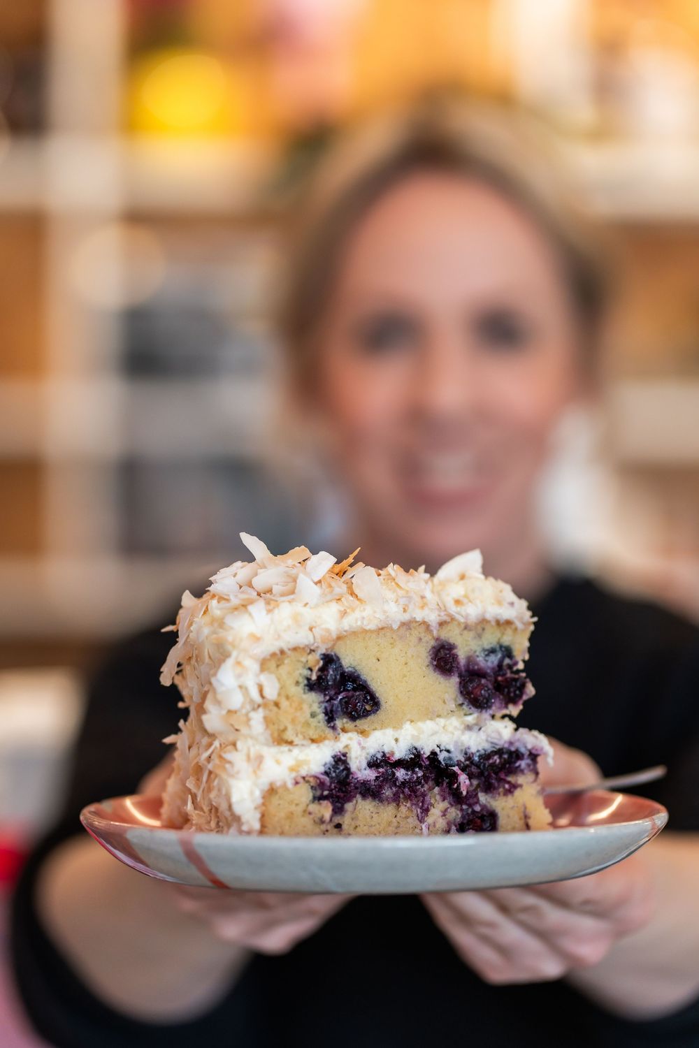 A slice of coconut-topped blueberry layer cake with white frosting sits on a blue plate.