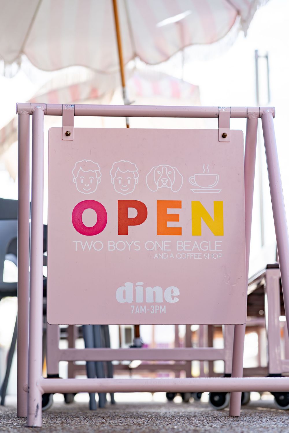 A pink open sign for 'Two Boys One Beagle' dine establishment mounted on a pastel frame stand.