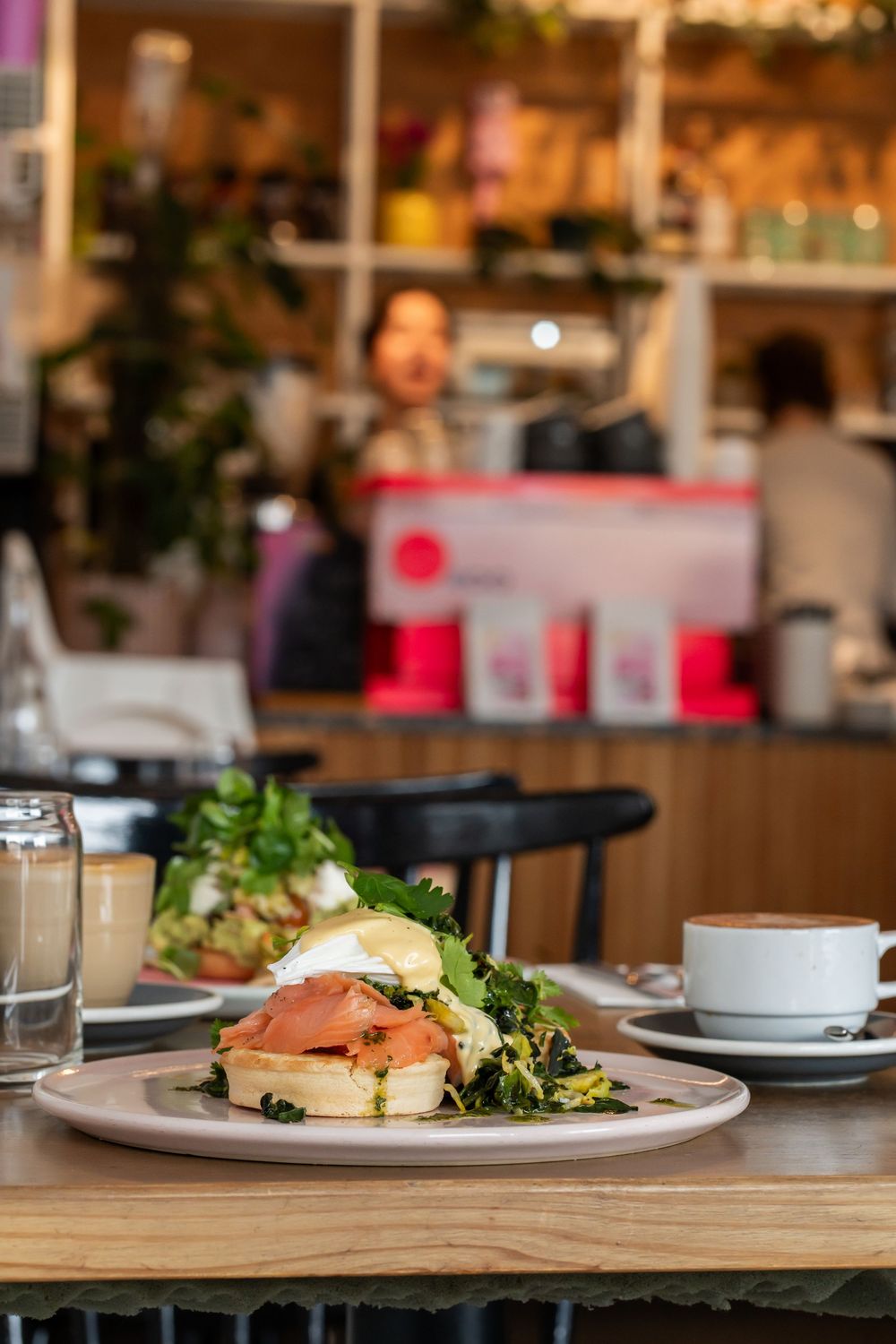 Three plates of eggs benedict with salmon and hollandaise sauce on wooden tables in a trendy brunch restaurant setting.