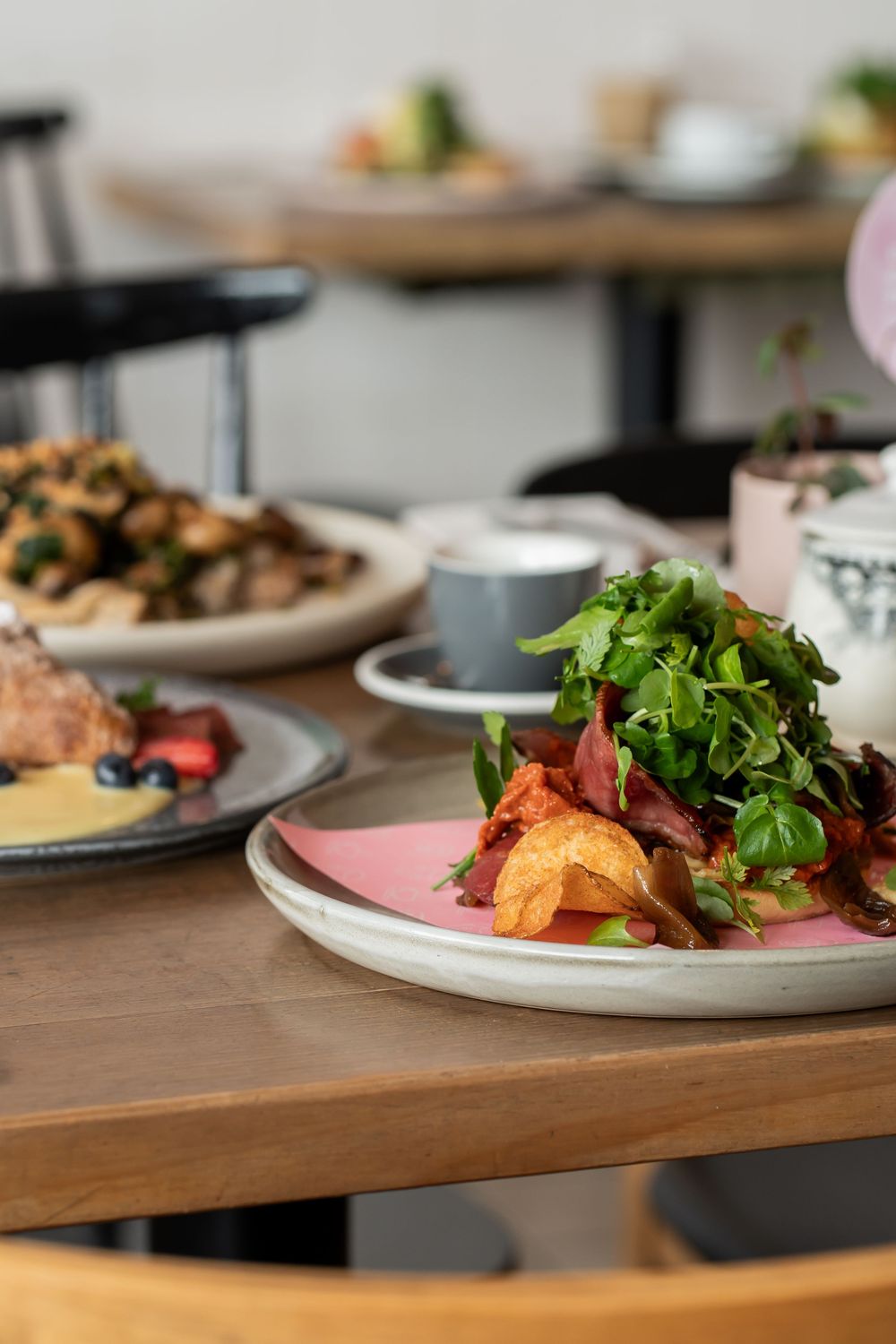 Fresh salad with crispy bacon and greens served on pink plate at wooden restaurant table alongside other dishes.
