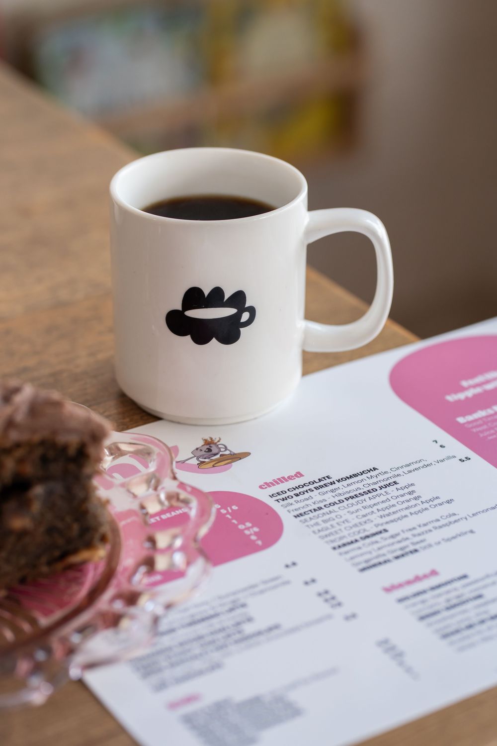 A white coffee cup sits beside a pink and white menu on a wooden table with soft lighting.
