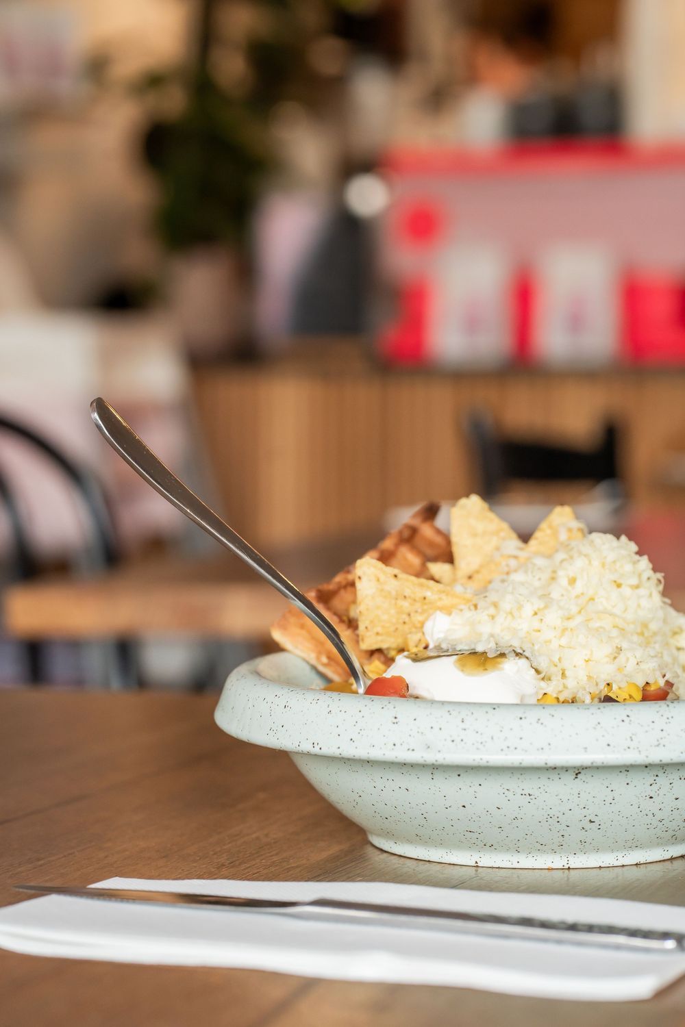 A ceramic bowl filled with shredded cheese and tortilla chips served on a wooden table in a casual dining setting.