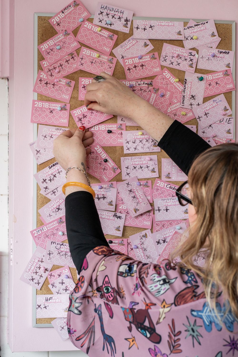 Person pinning pink notes onto a corkboard wall in decorative pattern taking multiple frames.