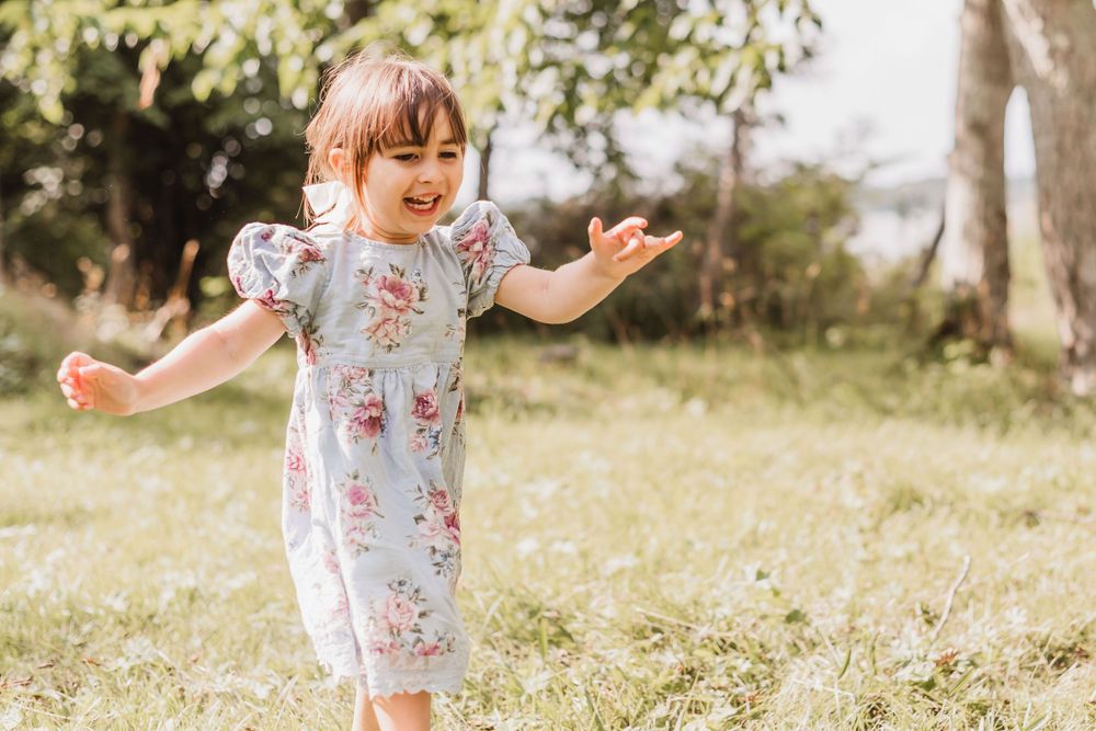 A child in a floral dress dances joyfully in a sunny meadow filled with wildflowers.