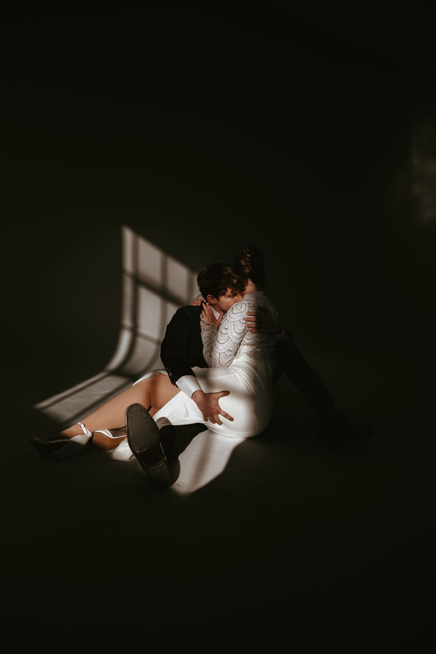 Artistic shadow play of couple in wedding attire sitting on floor.