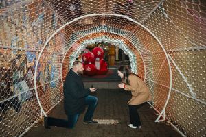 A couple shares a romantic moment under a tunnel of twinkling lights during proposal.