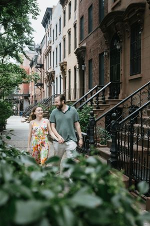Couple walking hand in hand down a charming brownstone-lined street in a historic neighborhood on a summer day.