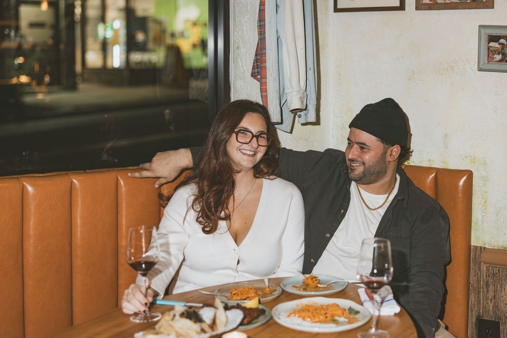 A group of people enjoying a meal together at a restaurant, sharing plates and drinks around a wooden table.