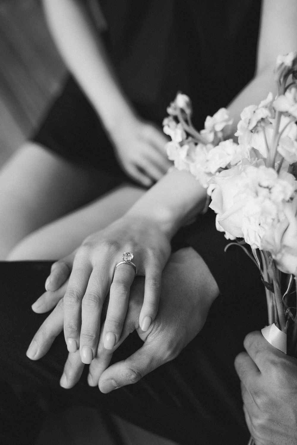 Black and white photo of couple holding hands with engagement ring and wedding bouquet.