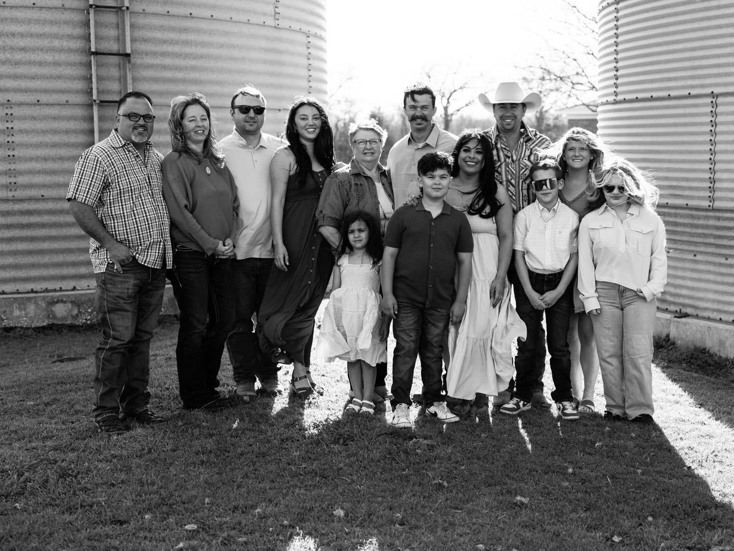 Black and white photograph showing a multigenerational family group posed together outside a house with siding.