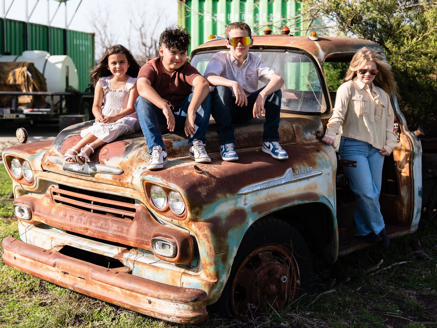 People posing together on a rusty vintage Chevrolet pickup truck in an outdoor setting.