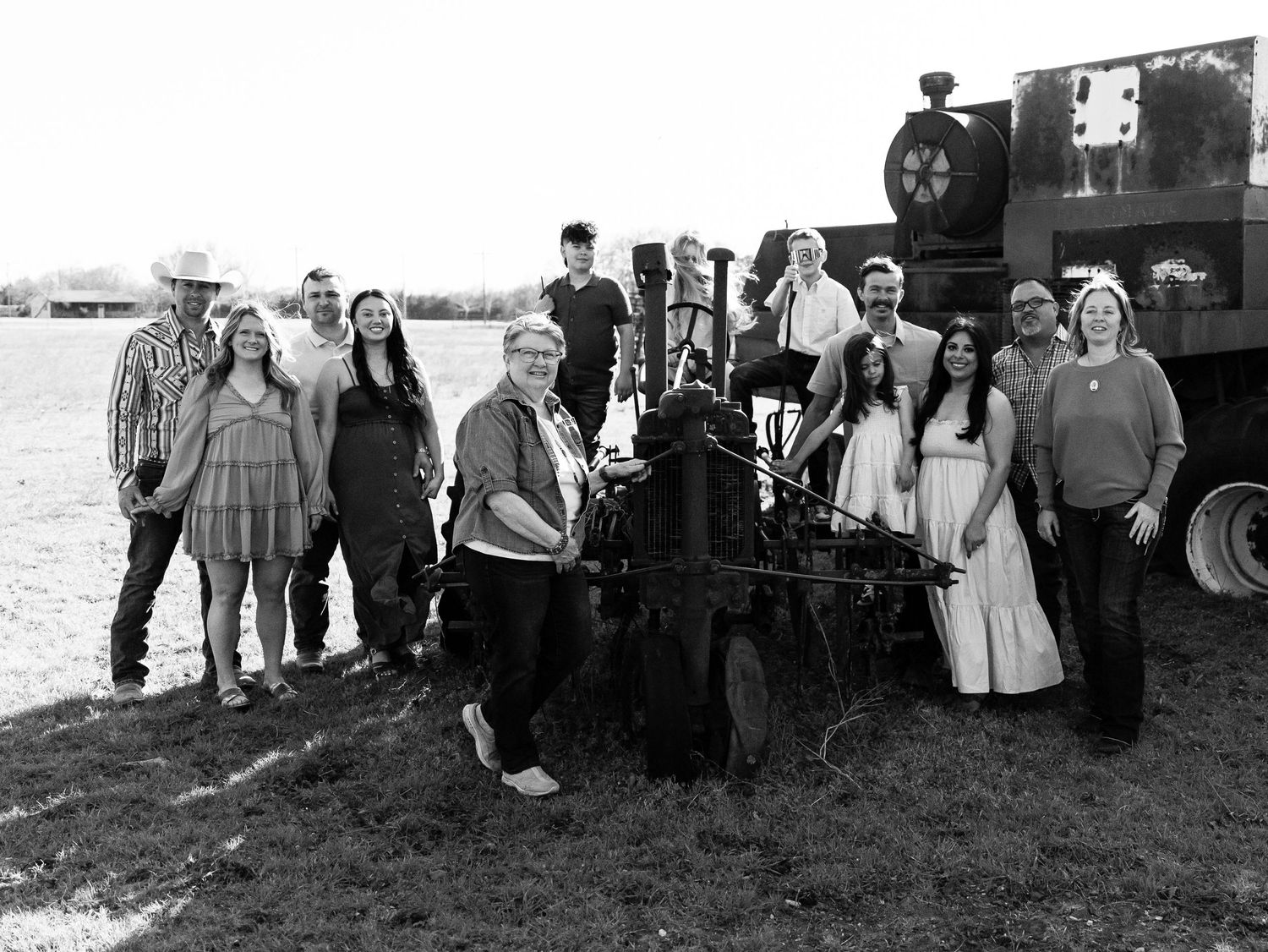 A black and white group photo of people gathered in front of a vintage steam locomotive in a rural setting.
