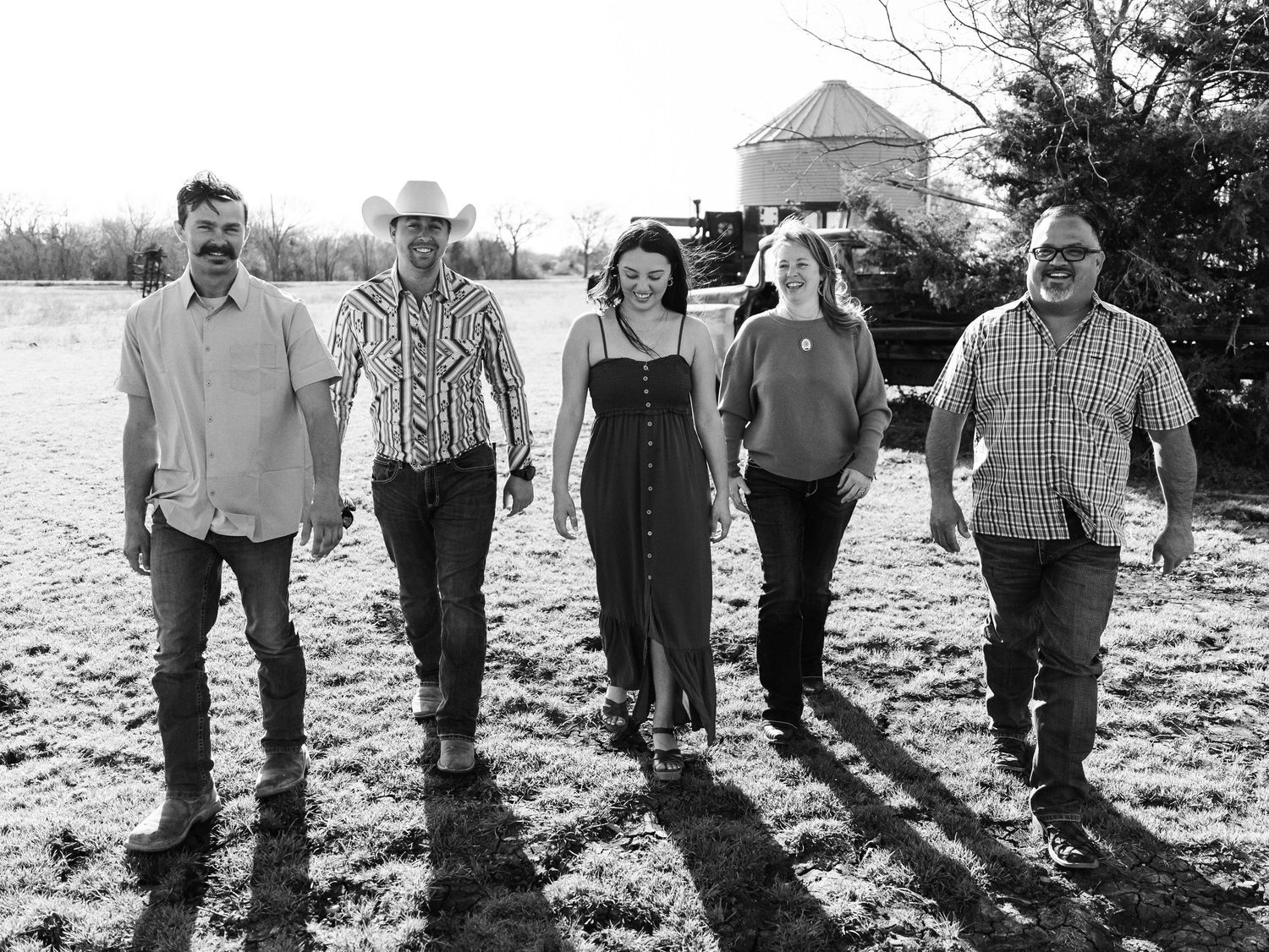 Black and white photo of five people walking together in a field with long shadows cast behind them in natural light.