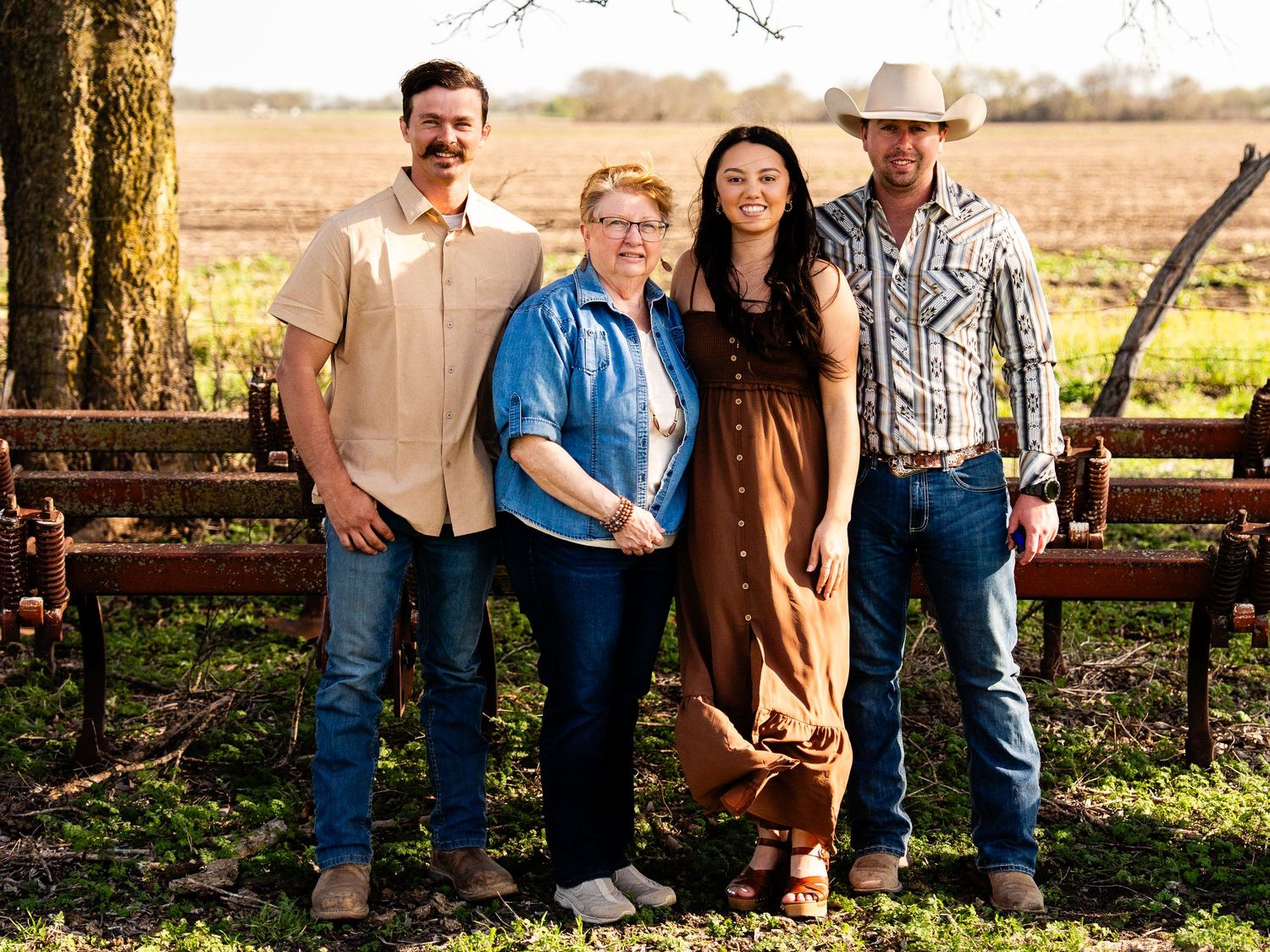 A group of four people pose together in front of a rustic wooden fence on a sunny autumn day in the countryside.