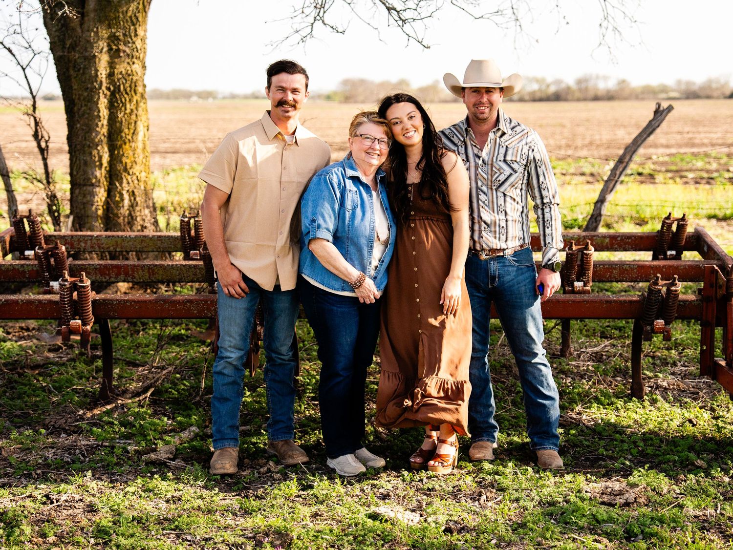 Rustic family portrait captured outdoors against vintage farm equipment at sunset in a rural countryside setting.