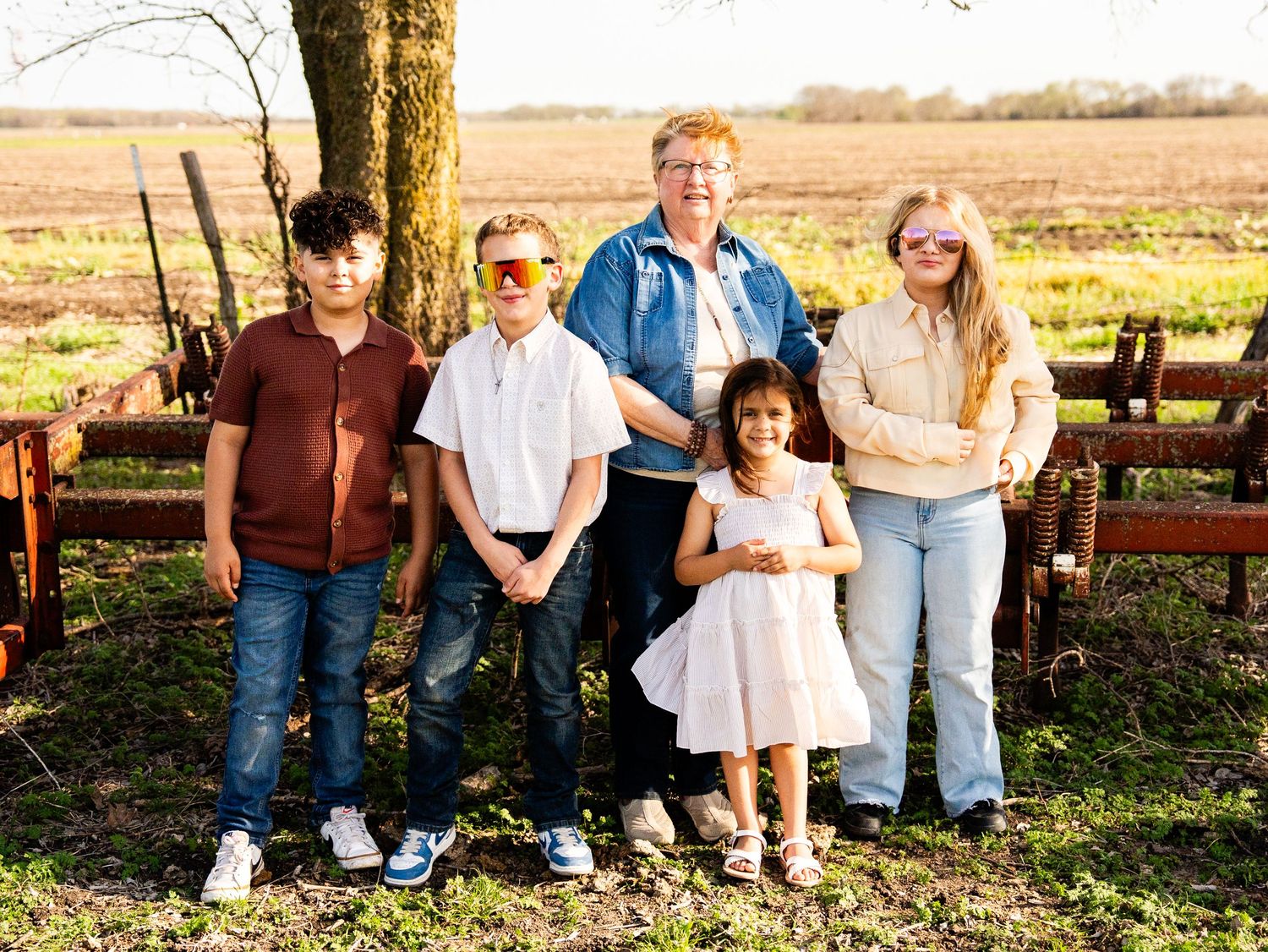 A group of people pose together outdoors near a wooden fence on a sunny autumn day in a rural setting.