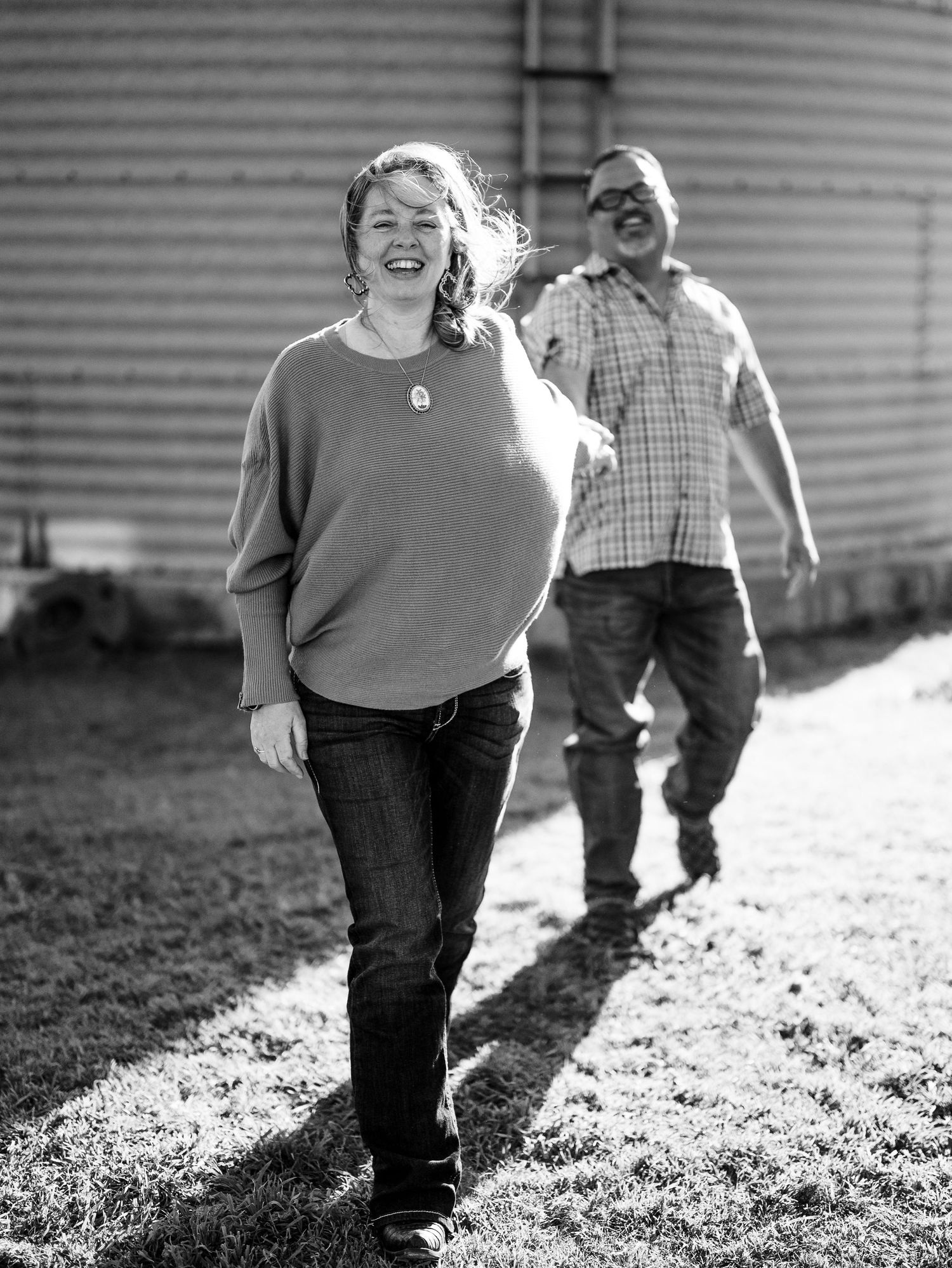 A candid black and white photograph of people sharing a joyful moment outdoors near farm silos on a sunny day.