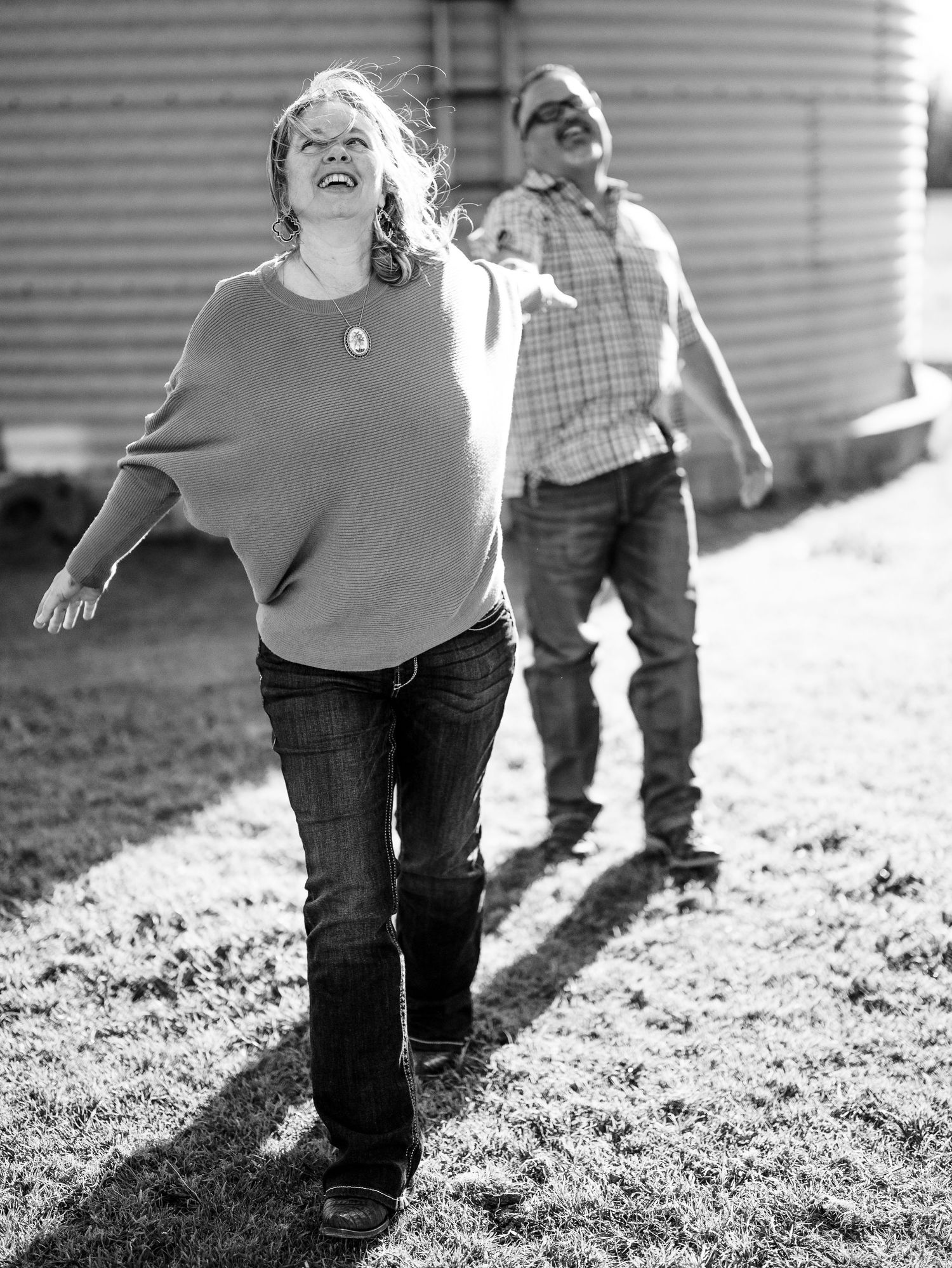Two companions share a joyful moment outdoors in black and white, with bright sunlight casting dramatic shadows.