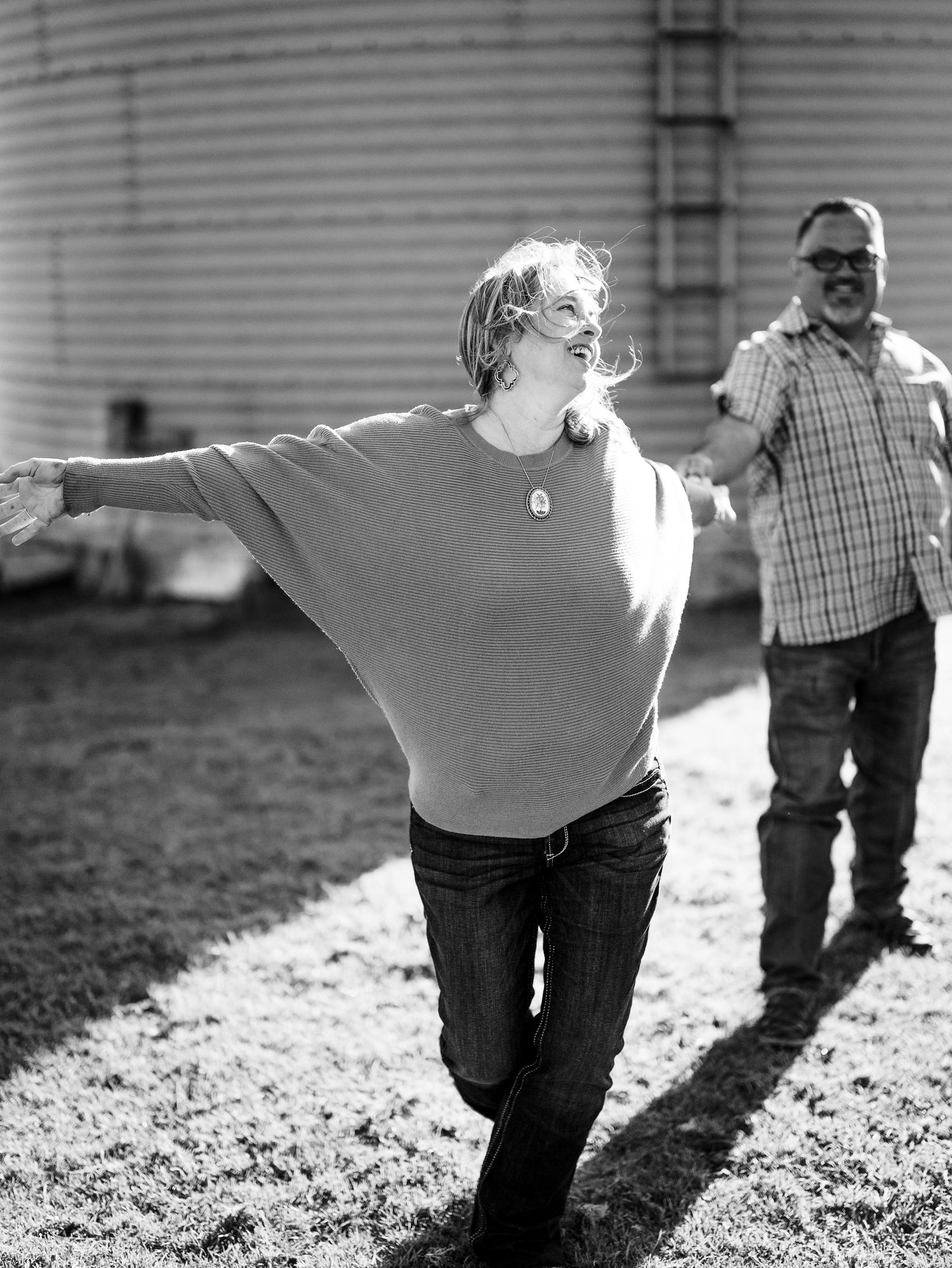 Black and white photo of two people enjoying a carefree moment outdoors by a grain silo.