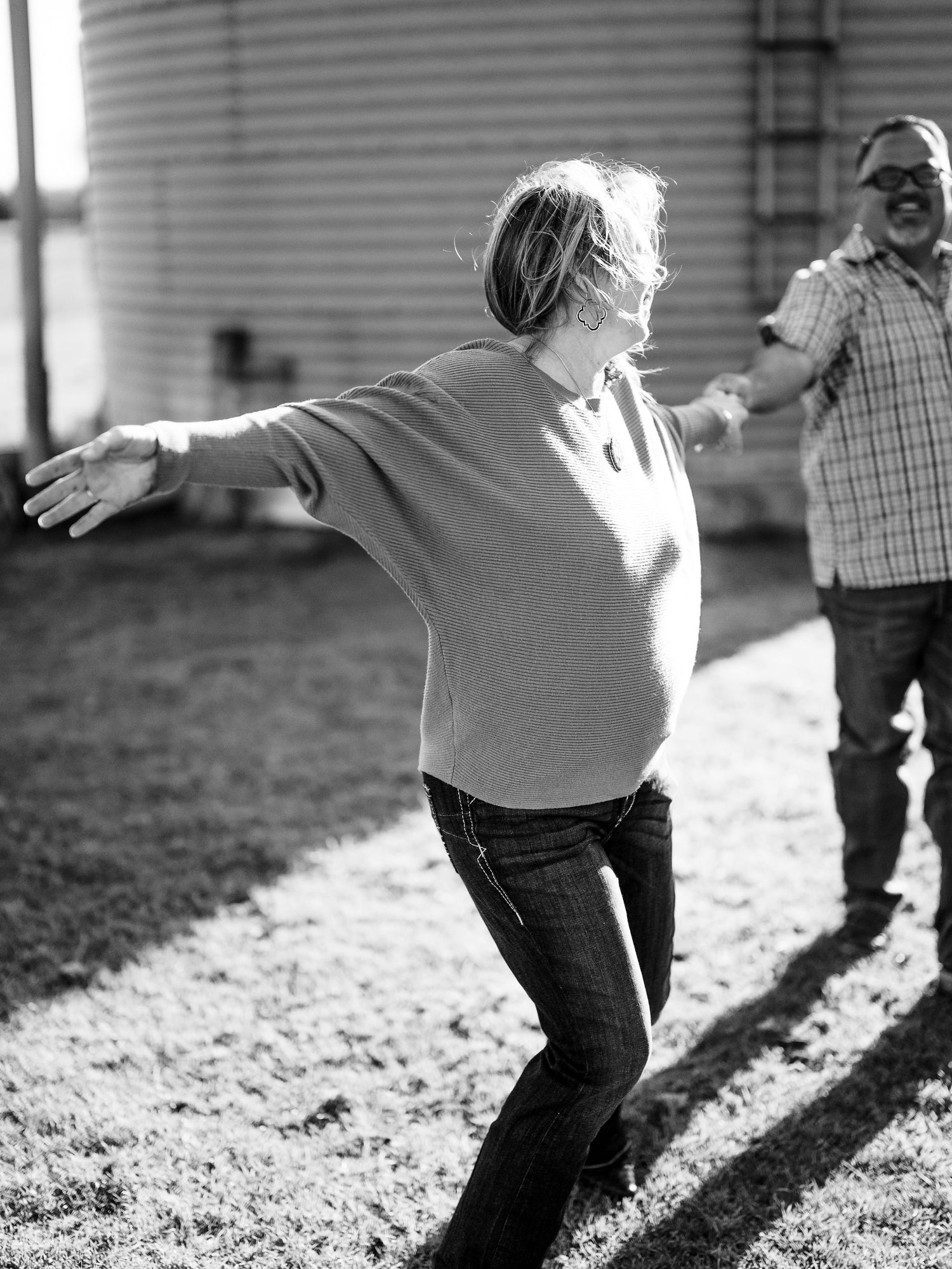 A candid black and white photo of two people joyfully playing outside on a sunny day, their shadows visible on the ground.