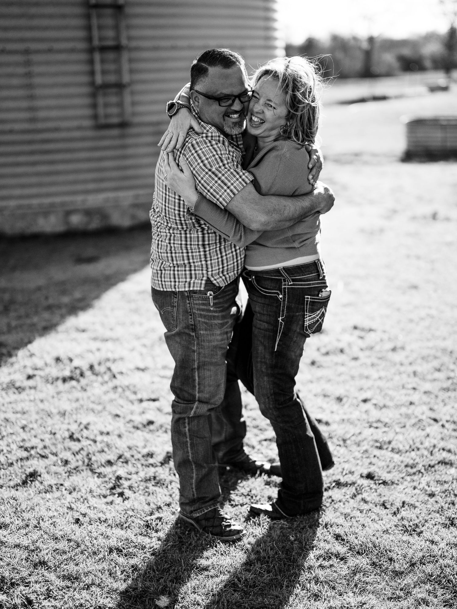 Black and white photo of a joyful couple embracing and laughing together outdoors in casual attire.
